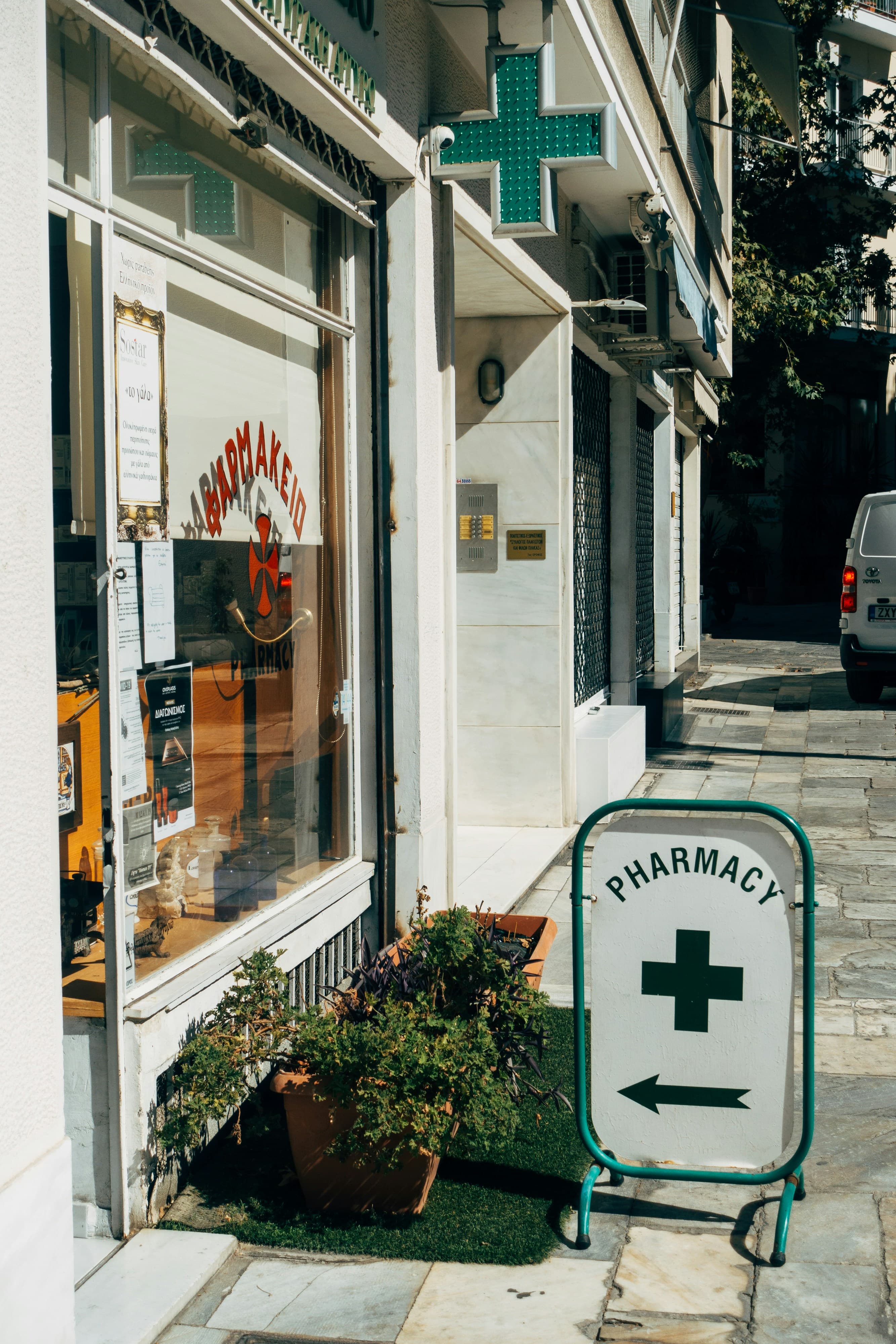 Ingresso di una farmacia di quartiere con croce verde e cartello sul marciapiede
